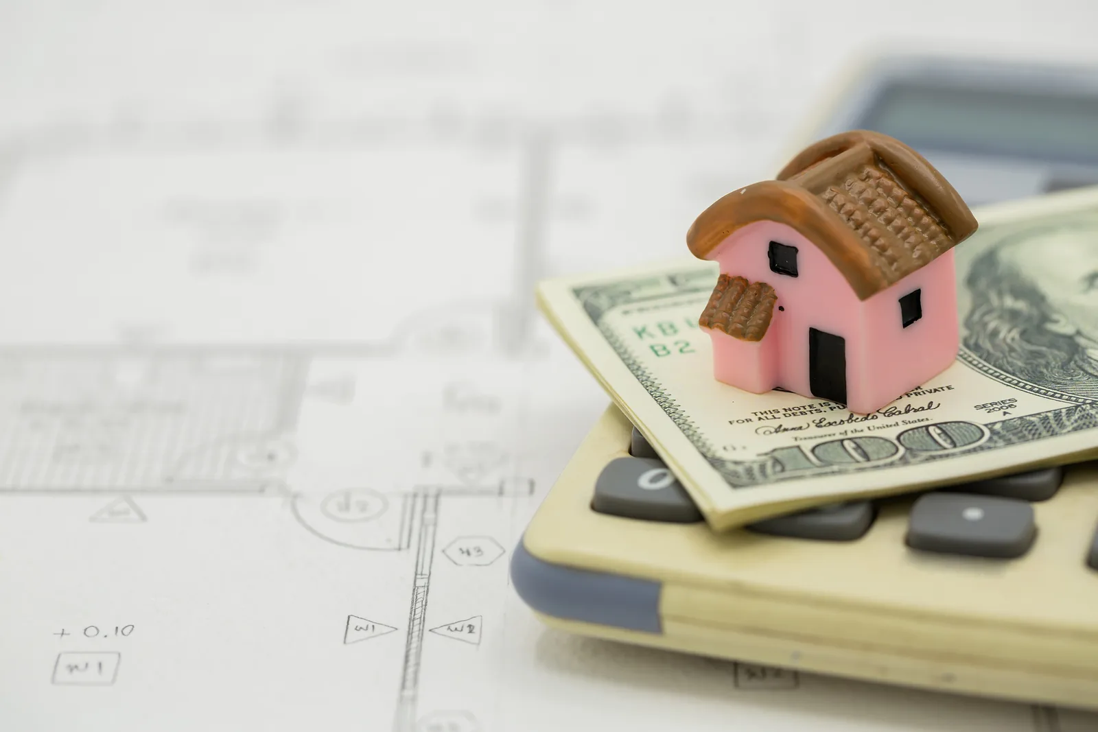Casa en miniatura sobre billetes y una calculadora para estimar cuánto puede pagar por una vivienda