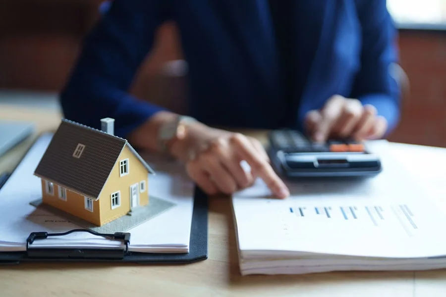 Una compradora calculando los gastos de la compra de una vivienda junto a una casa en miniatura