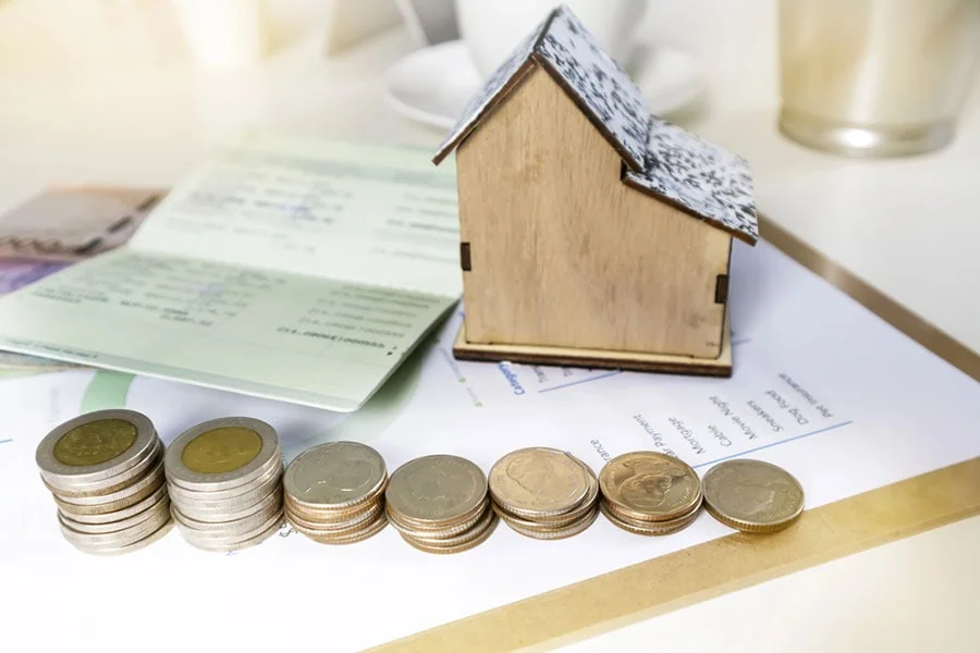 Una casa en miniatura, documentos de cierre y monedas que representan los gastos de bolsillo al comprar una vivienda